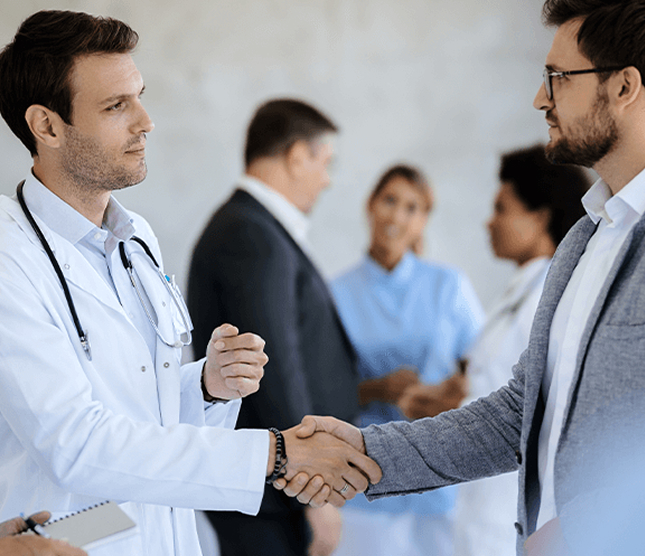 Two healthcare professionals shaking hands while colleagues talk in the background