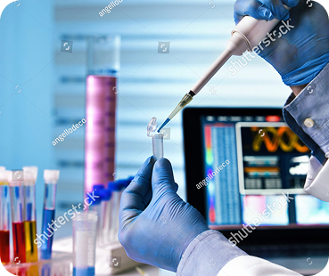 Researcher pipetting a sample beside laboratory analysis screens